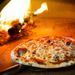 Close up pizza in firewood oven with flame behind
