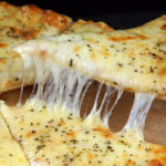 Hot appetizing cheese pizza, cut into pieces, one of which is picked up.